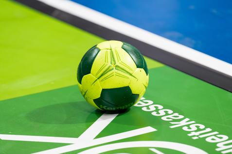 Grüner und gelber Handball liegt auf einer grünen Spielfläche mit weißem Schriftzug.